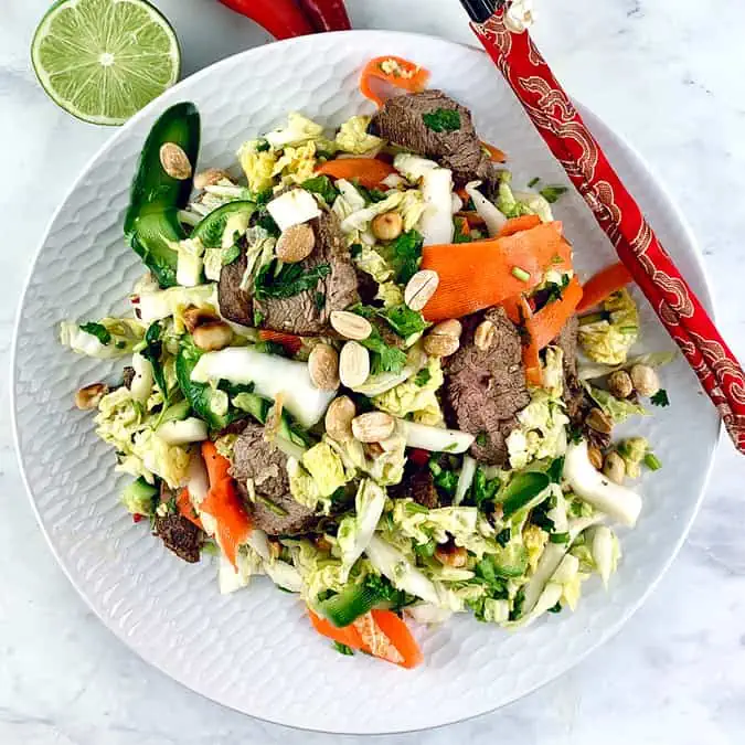 Vietnamese Beef Salad on a white plate with red chopsticks on the side, half a lime and chilli.