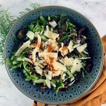 Balsamic mushroom salad with shaved parmesan. With a orange linen napkin on the right and rosemary sprigs on the left.