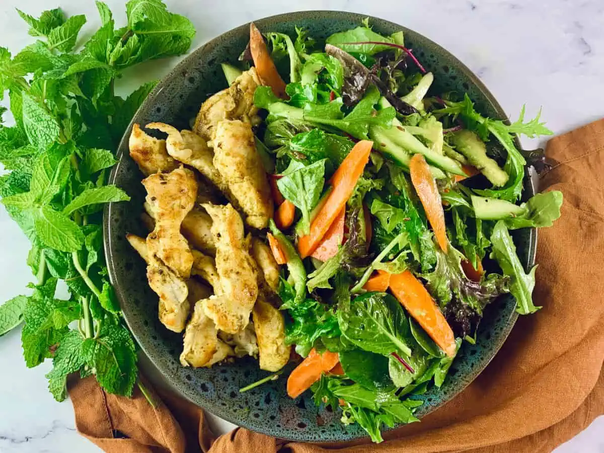 Keto Curry Chicken Salad in a dark grey patterned bowl with an orange linen napkin at bottom right corner and mint leaves on left.