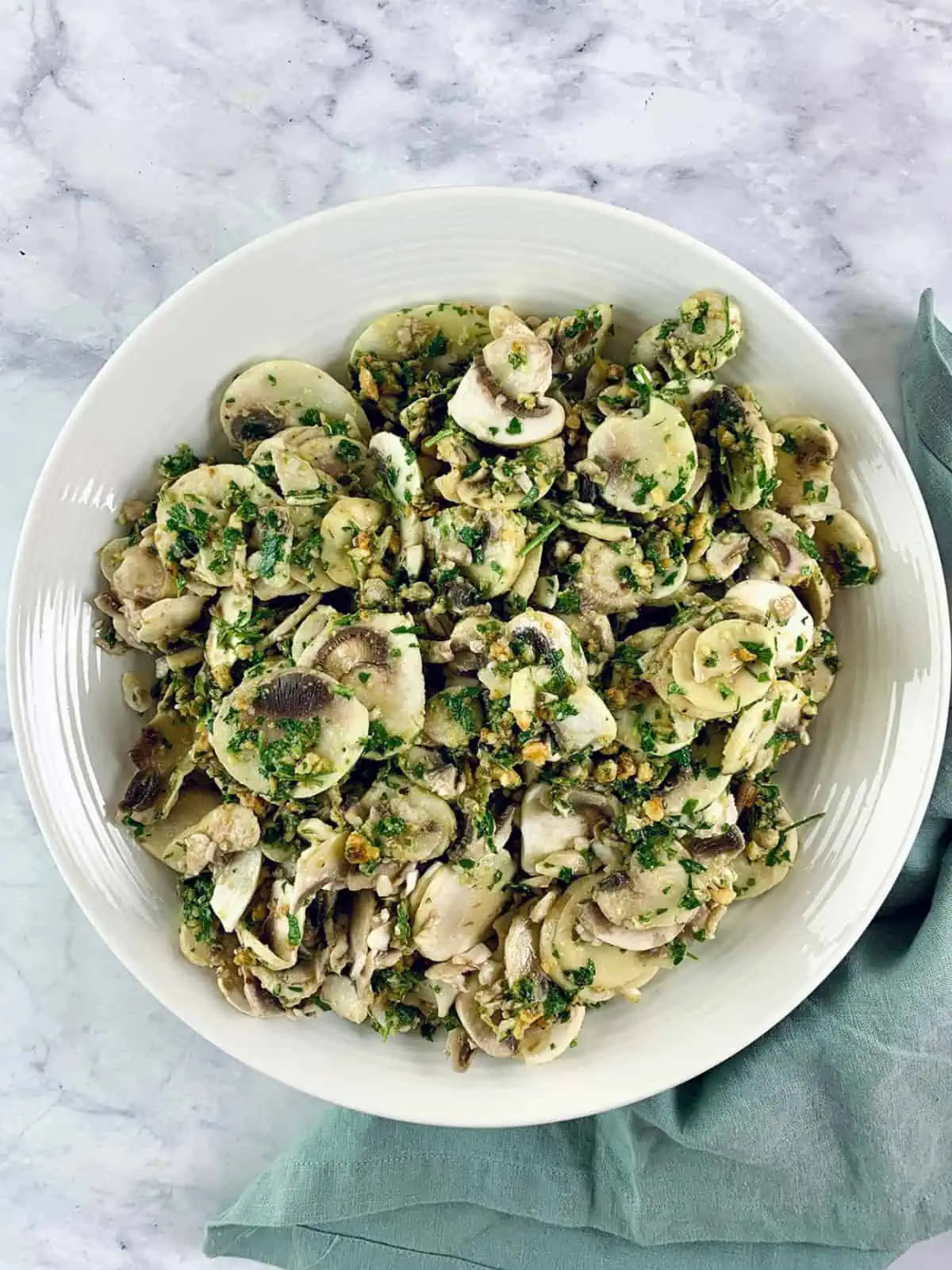 Raw mushroom salad with hazelnut gremolata in a white bowl, with a mint linen napkin on the left.