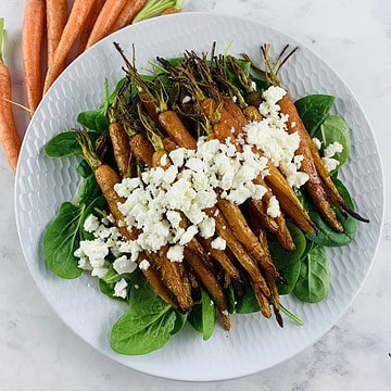 Honey Harissa Carrots on a white plater with baby carrots on the side.