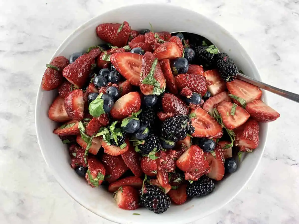 Mixing a summer berry salad in a white bowl with a spoon.