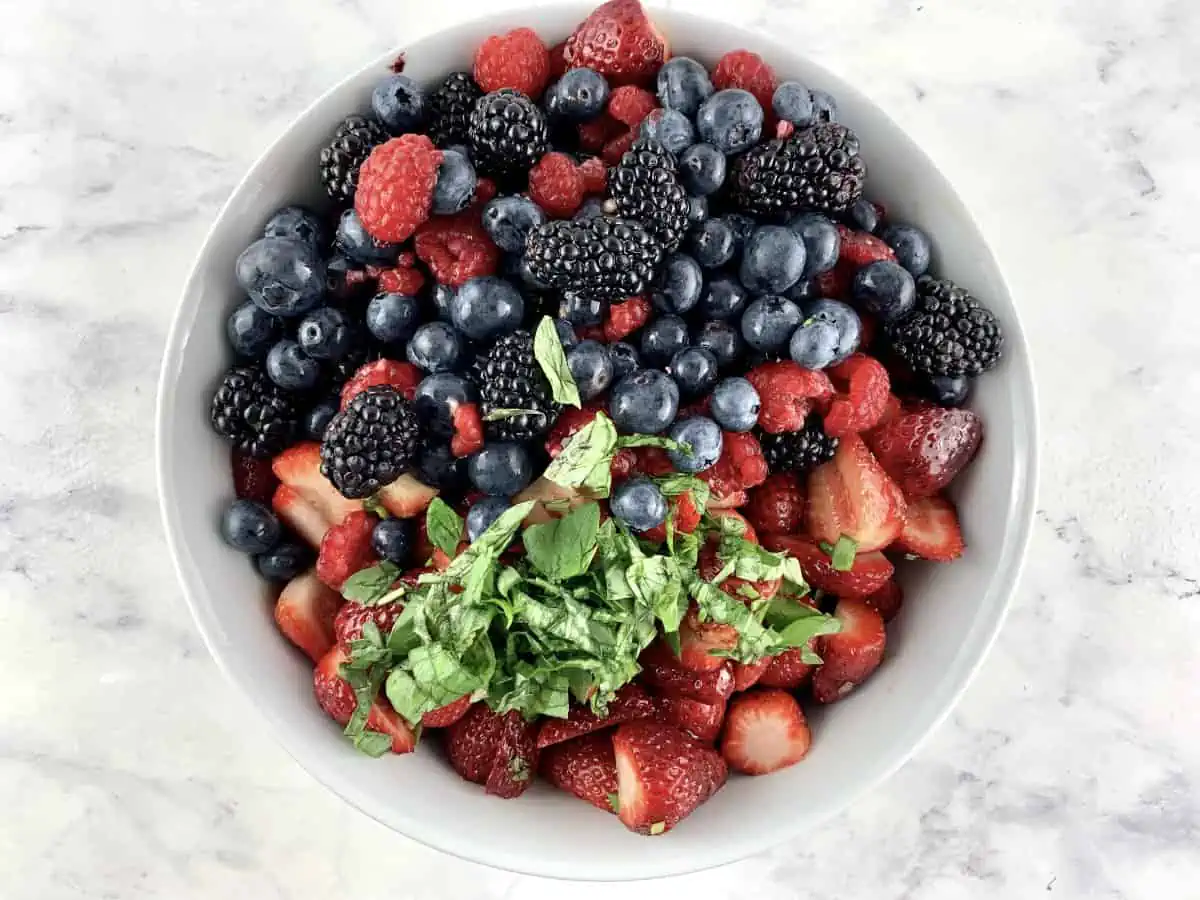 Prepared ingredients for summer berry salad in a white bowl.