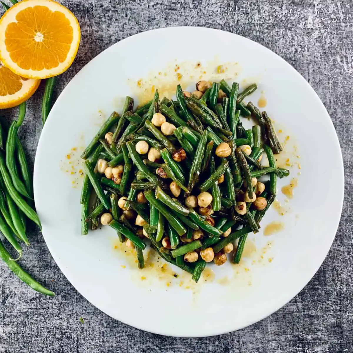 Green bean salad with orange and hazelnuts in a white platter with orange slices & beans on the side.