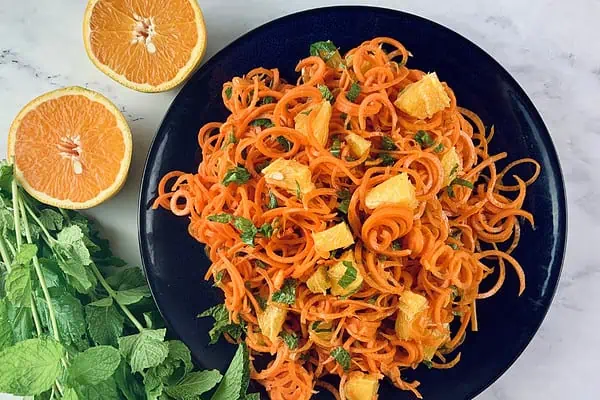 A spiral carrot & orange in navy plate with orange slices and mint sprigs on the side salad.