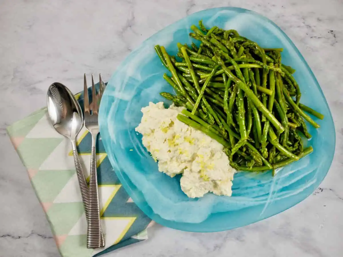 Baby asparagus and lemon ricotta salad on an aqua platter with serving spoons on the side.