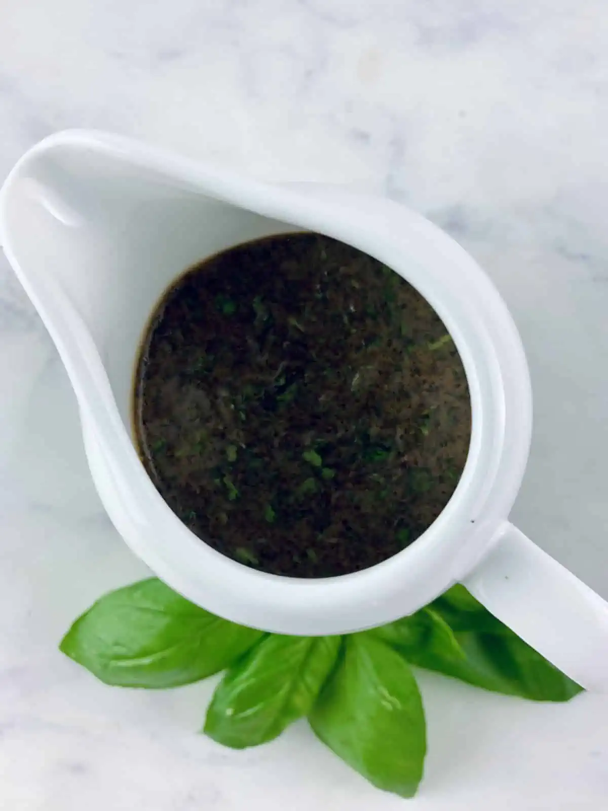 Basil balsamic vinaigrette in a white pouring jug with a basil sprig on the side.