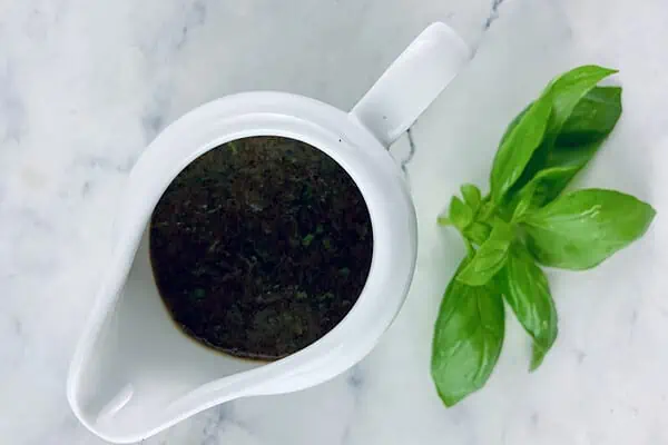 Basil balsamic vinaigrette in a white pouring jug with a basil sprig on the side.