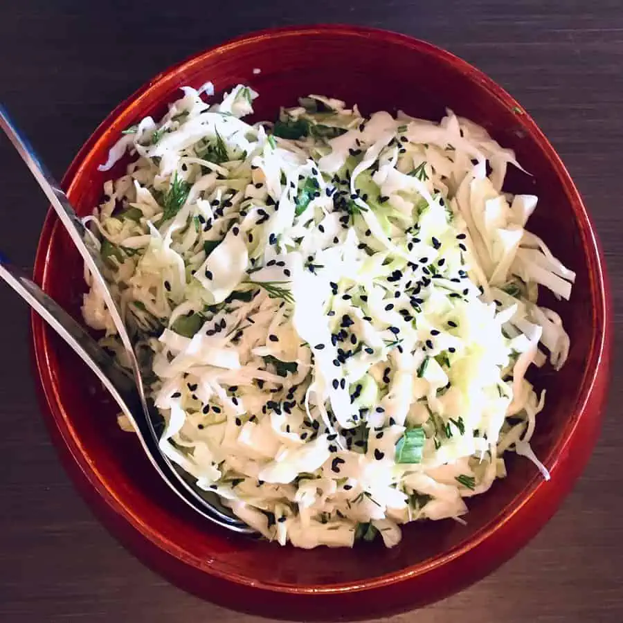Horseradish coleslaw in a red bowl with salad servers.