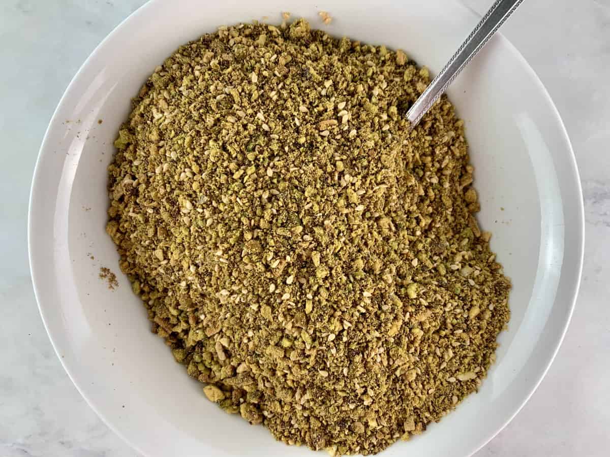 Mixing pistachio dukkah ingredients in a white bowl.