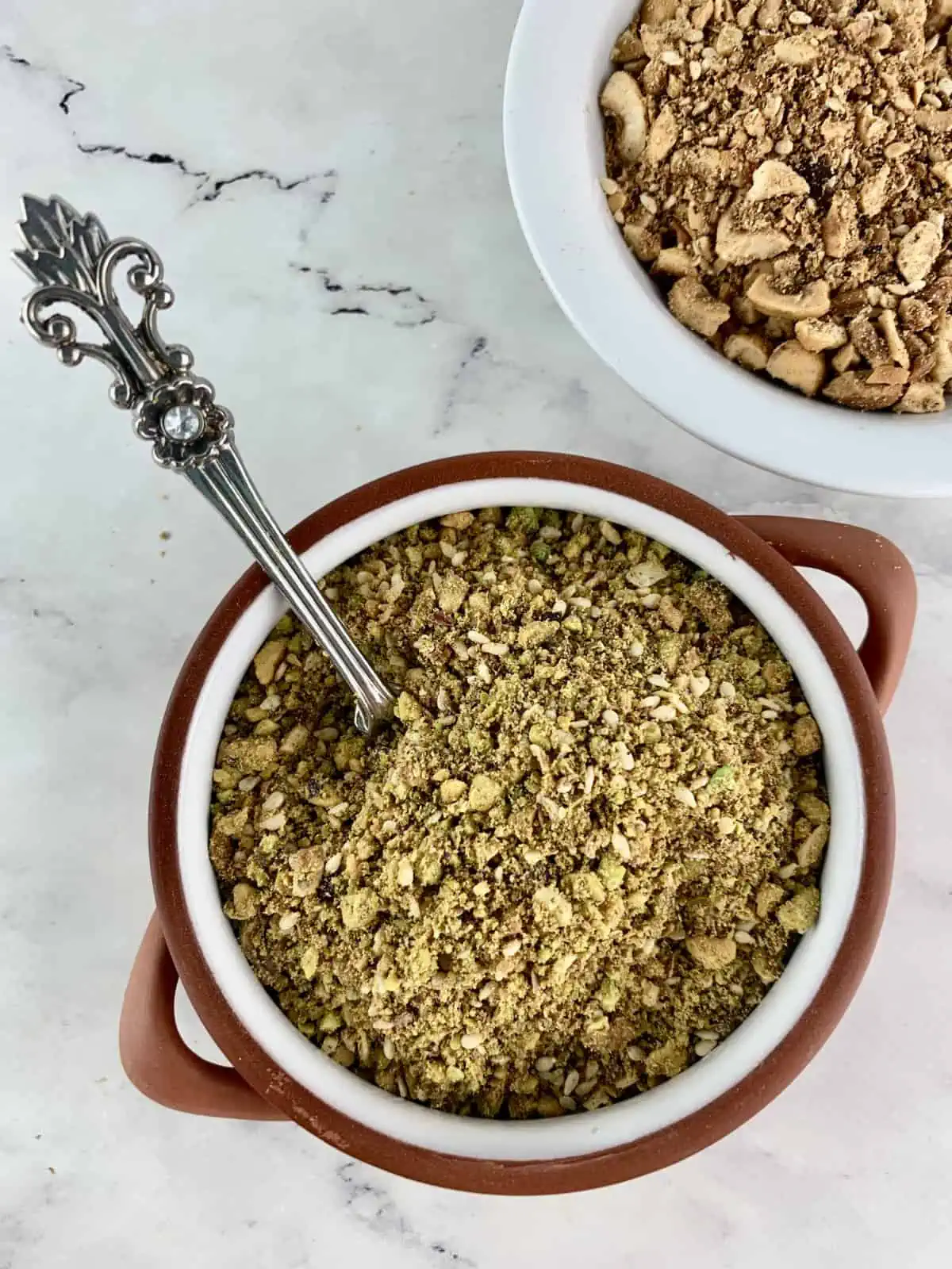 Pistachio dukkah recipe in a ceramic bowl with a spoon and nuts on the side.