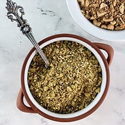 Pistachio dukkah recipe in a ceramic bowl with a spoon and nuts on the side.