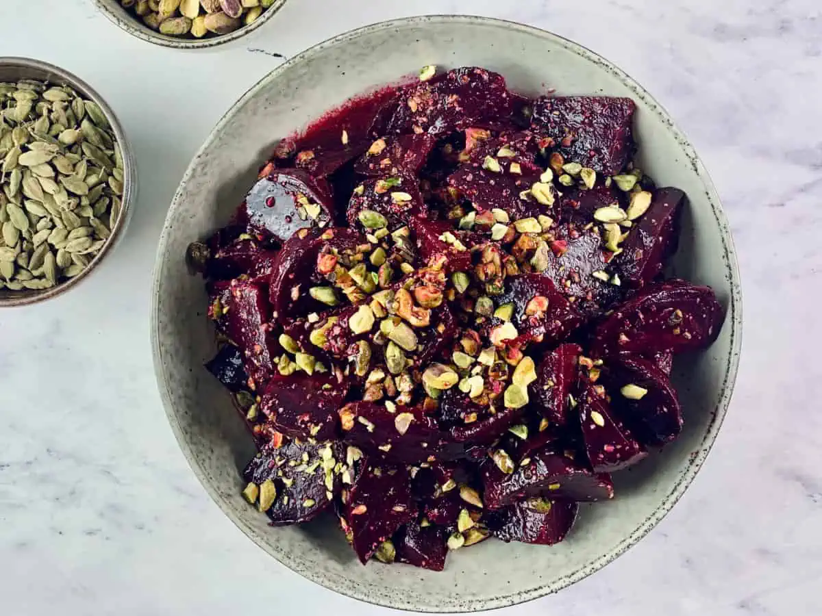 Roasted beet salad in a bowl, with cardamom and pistachios in bowls on side.