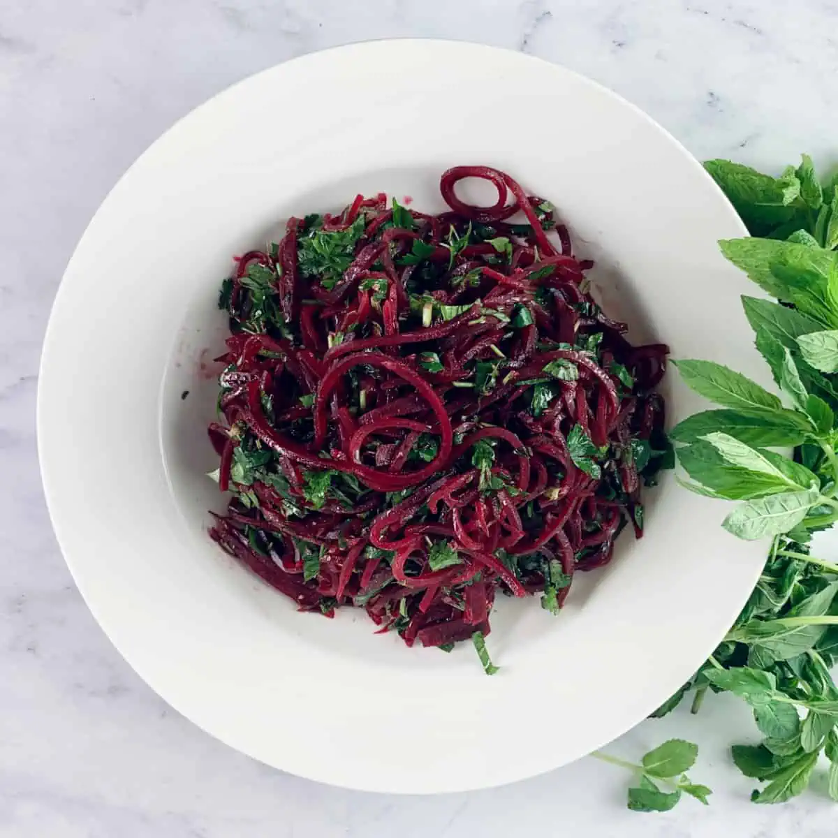 Spiralized beetroot salad in a white bowl with mint on the side.