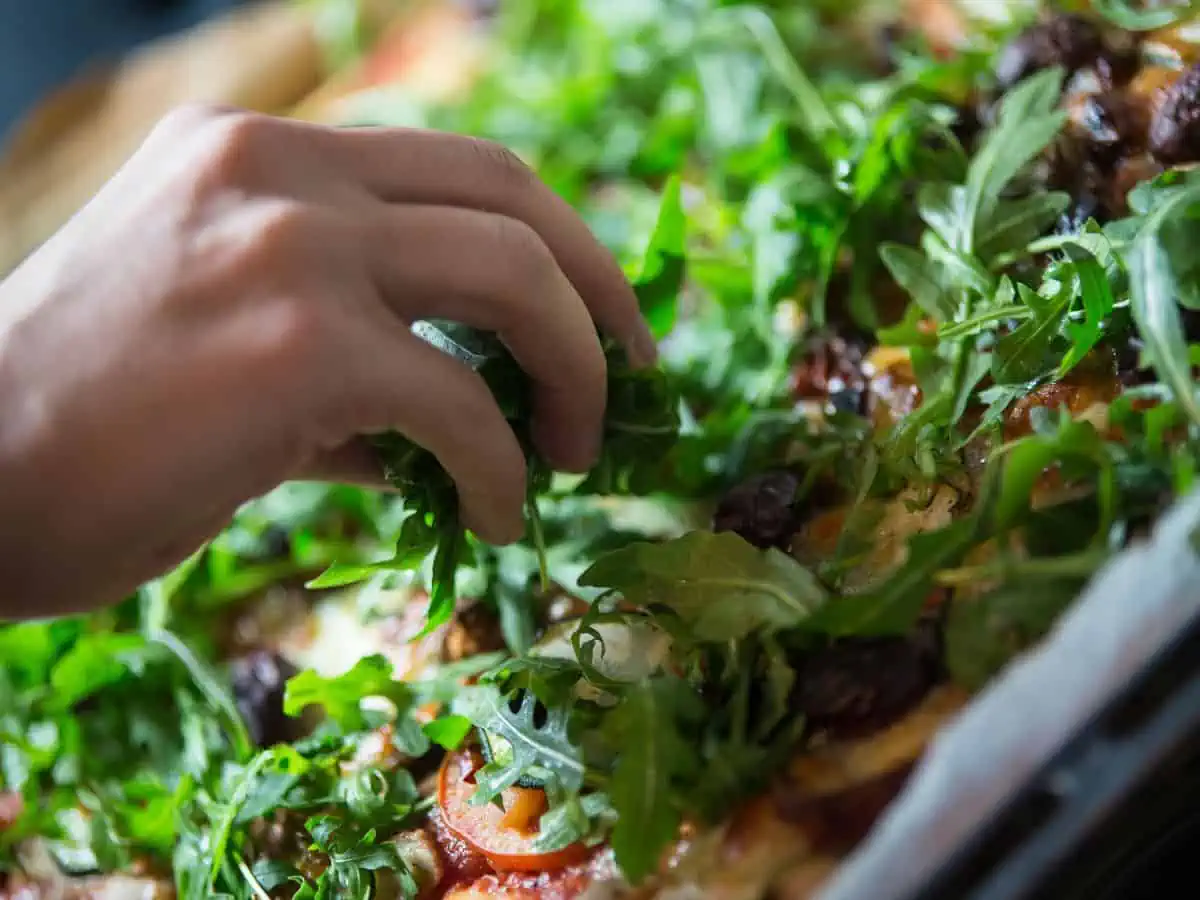 Scattering rocket/arugula on top of a pizza.