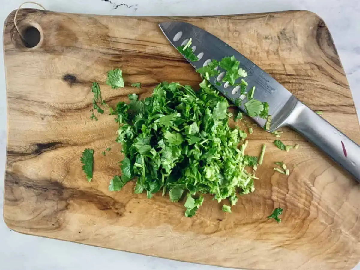 Chopped coriander or cilantro on a wooden board with a knife.