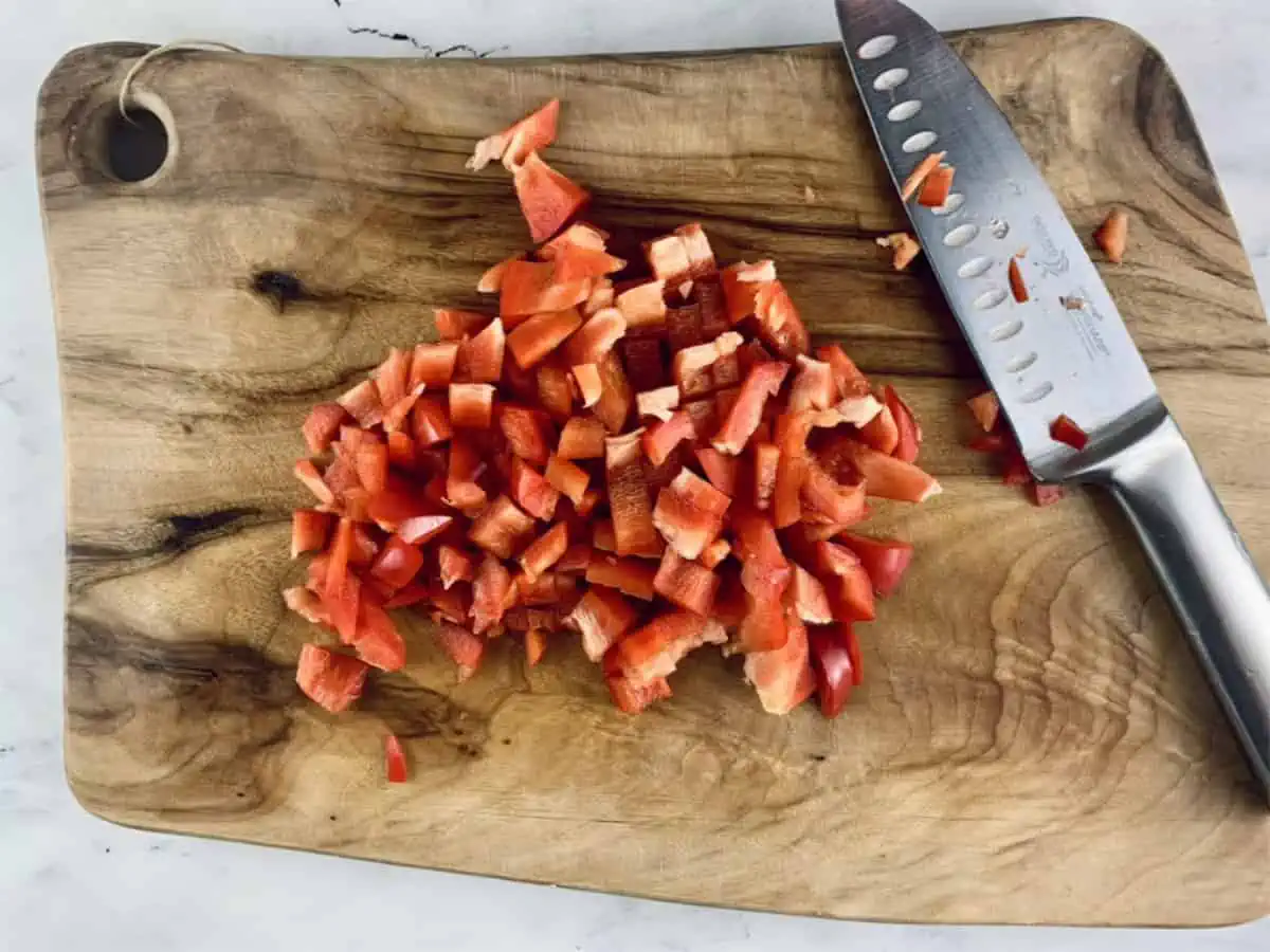 Diced red pepper or capsicum on a wooden board with a knife.