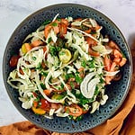 A close up of Fennel and Tomato Salad in a dark grey bowl with an orange linen napkin on the side.