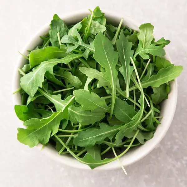 An aerial view of rocket/arugula in a white bowl.