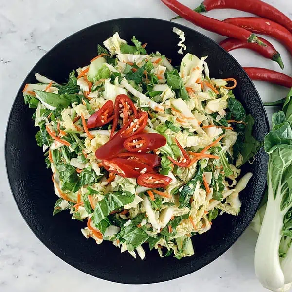 Asian wombok salad with a chilli garnish on a black platter with bok choy leaves and chillies on the side.