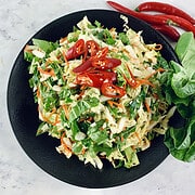 Asian wombok salad with a chilli garnish on a black platter with bok choy leaves and chillies on the side.