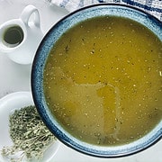 Oregano vinaigrette in a small blue ceramic bowl with dried oregano, sprigs and a small olive oil jug on the side.