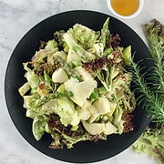 Red leaf salad on black plate with red lettuce leaves and rosemary stems on the side as well as a small bowl with honey.