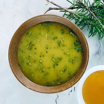 Rosemary vinaigrette in a tan bowl with honey and rosemary sprigs on the side.